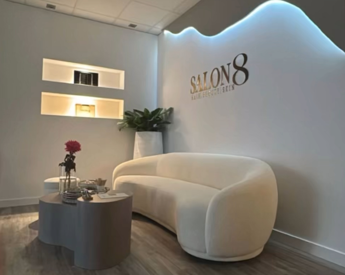 De wachtruimte van Salon8: een ronde crèmekleurige bank voor de verlichte wand met het SALON8-logo